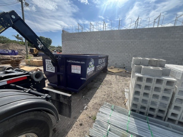 Chickadee Dumpster Rental 15-yard dumpster on-site at a new Kia dealership construction project in Fort Pierce, Florida. The roll-off dumpster is being used for commercial construction debris removal during the dealership build