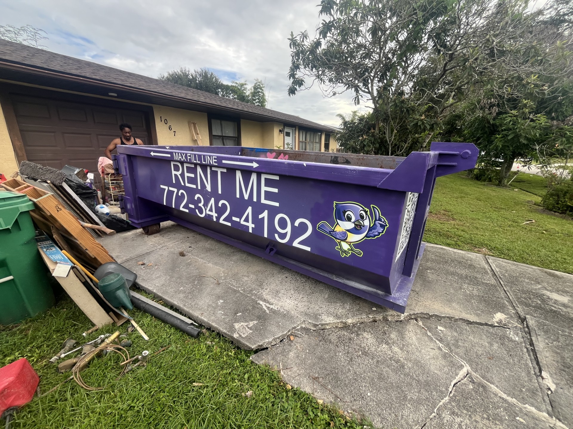 Purple Chickadee Dumpster Rental roll-off dumpster in a residential driveway with wood scraps, furniture, and household debris being cleared from a home. what to throw away before selling a house
